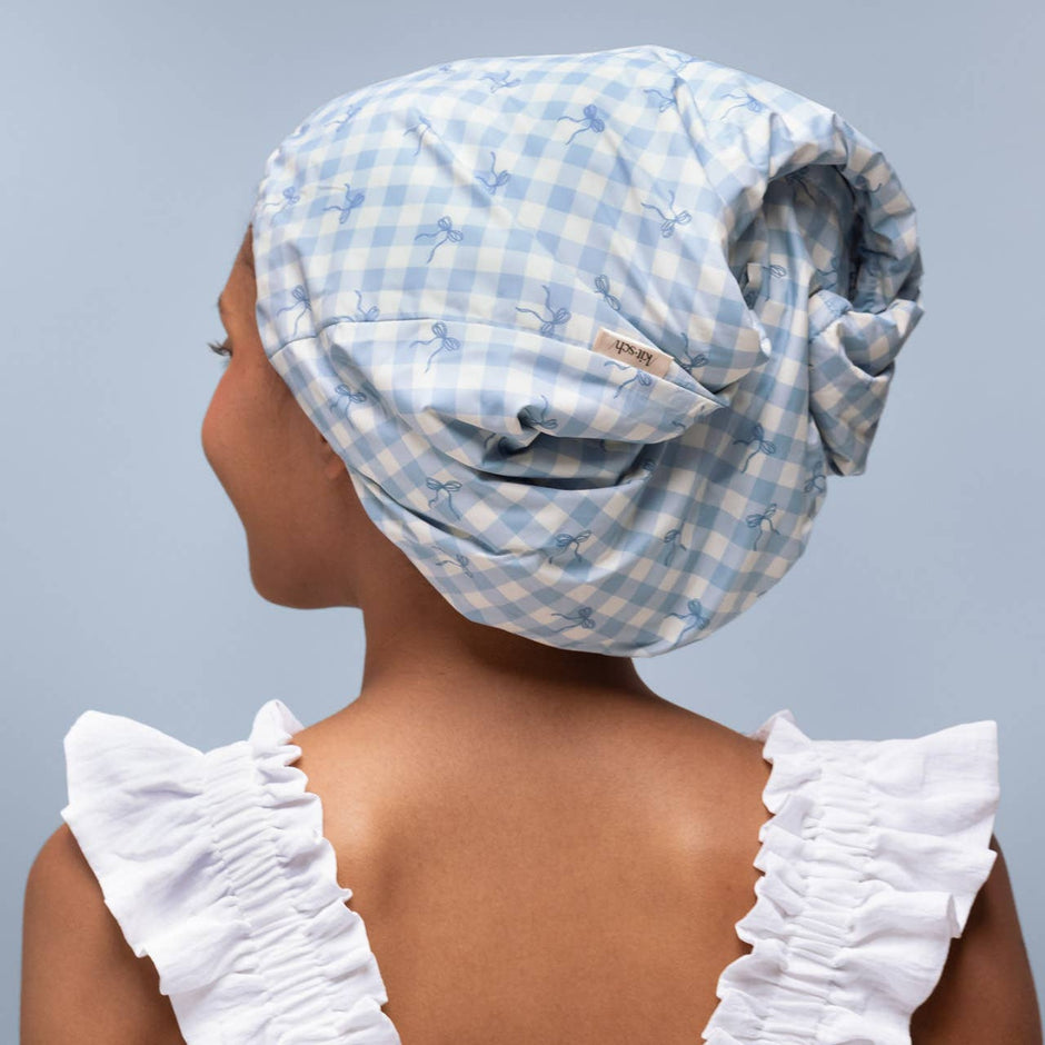 Woman wearing blue gingham satin-lined shower cap with white ruffled sleeves