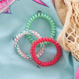Three colorful spiral hair ties displayed on light blue fabric with cream knit accessories