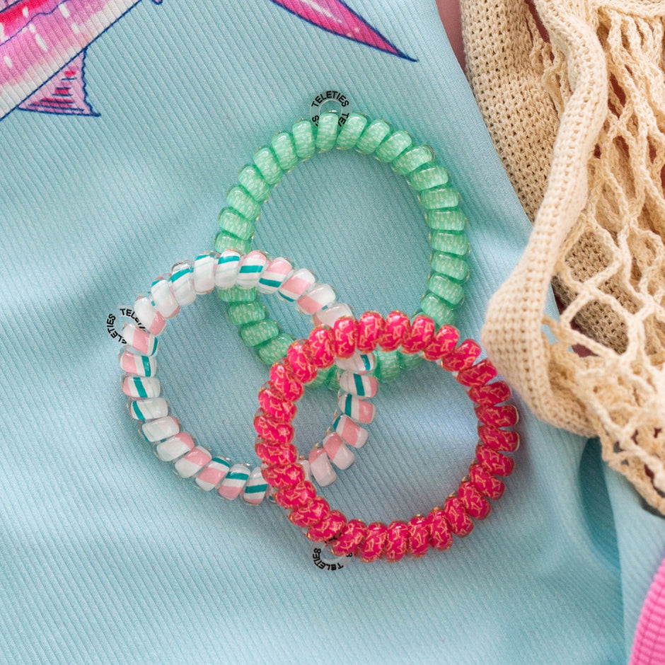 Three colorful spiral hair ties displayed on light blue fabric with cream knit accessories