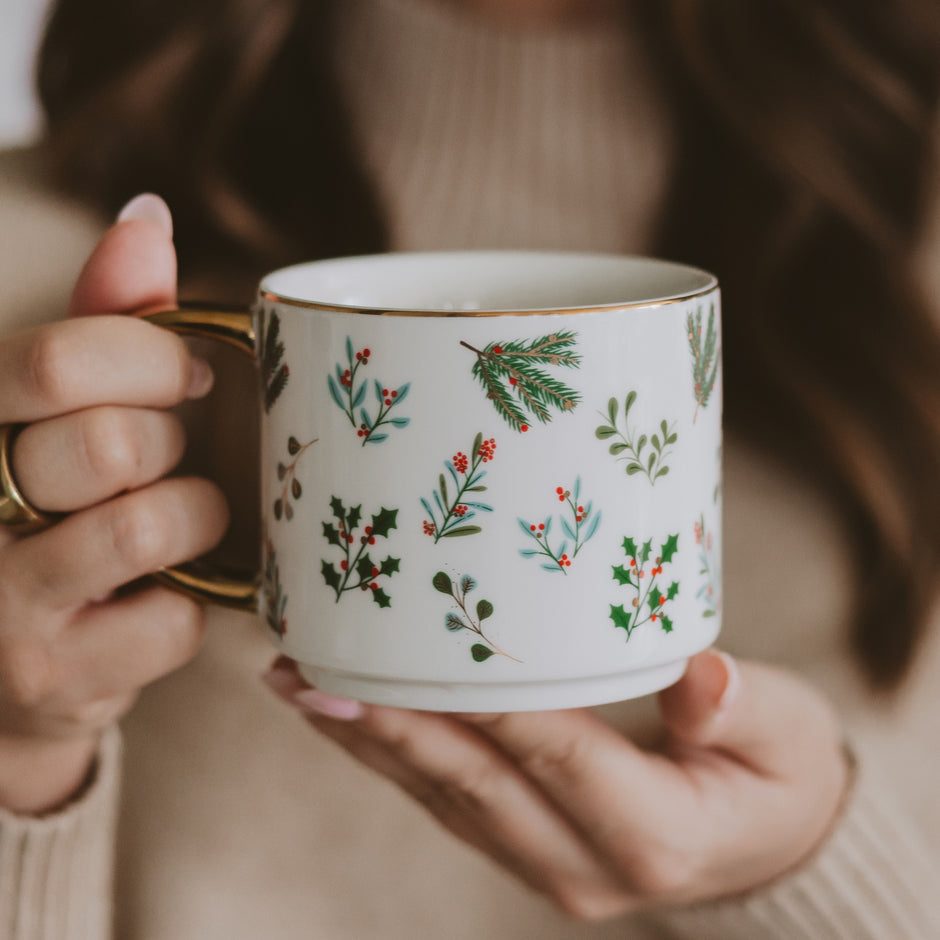 Holiday Greenery Coffee Mug held in hands, featuring festive pine and holly designs with gold rim