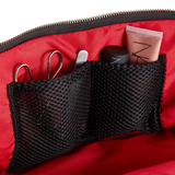 KUSSHI | Vacationer Makeup Bag — Black/Red, Close-up of the inside of a red makeup bag or cosmetic pouch, showing black mesh organizer pockets holding scissors, a small white tool, a black item, and a pink tube. A black zipper is visible along the top.