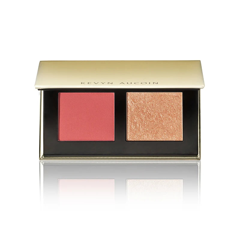 Kevyn Aucoin two-pan makeup palette with a gold lid and black base, featuring a matte coral pink blush and a shimmering champagne-gold highlighter, shown on a white background with a reflection.