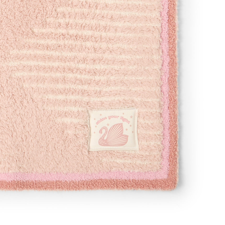 Detail of pink blanket with swan patch that reads "shine your light"