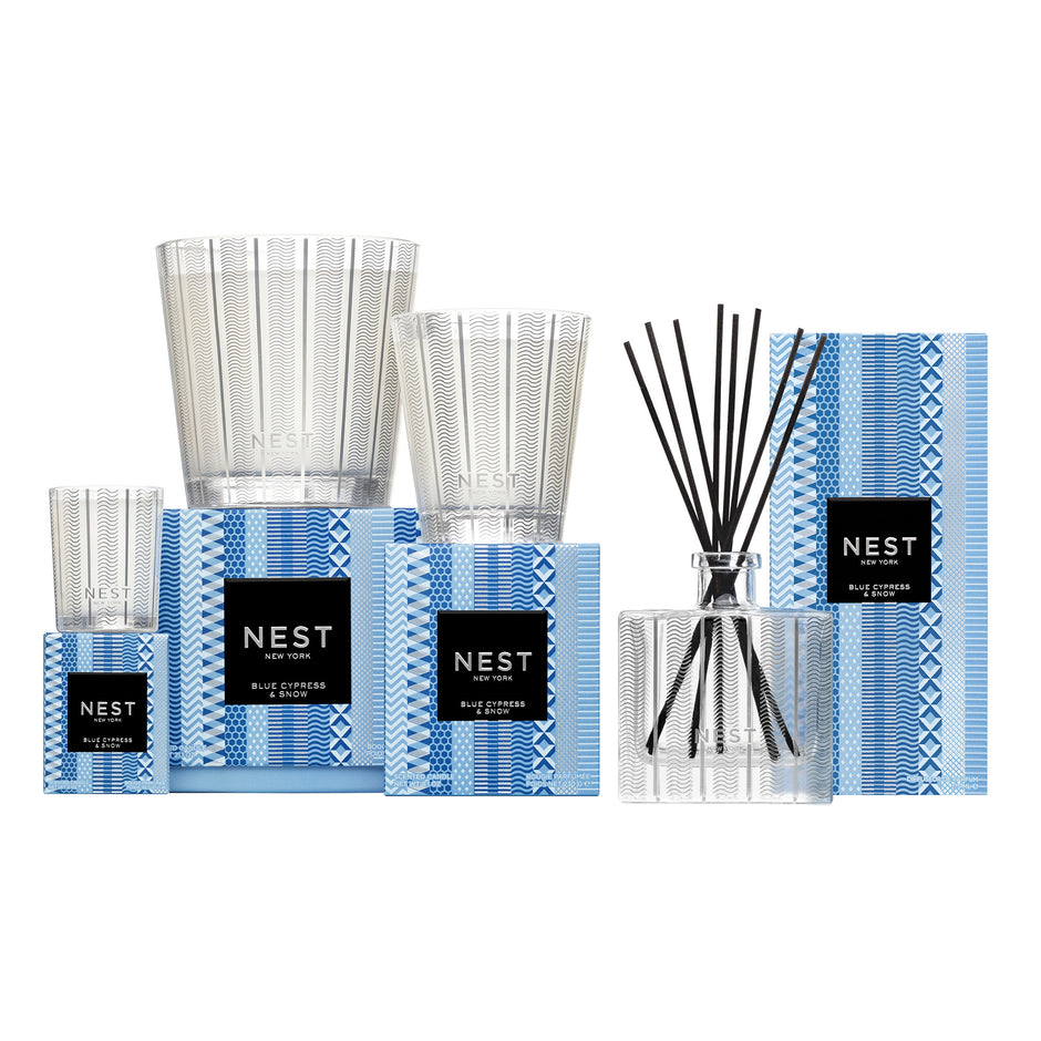 A NEST New York Blue Cypress & Snow collection of candles and a reed diffuser on a white background, each paired with a blue and white patterned box.