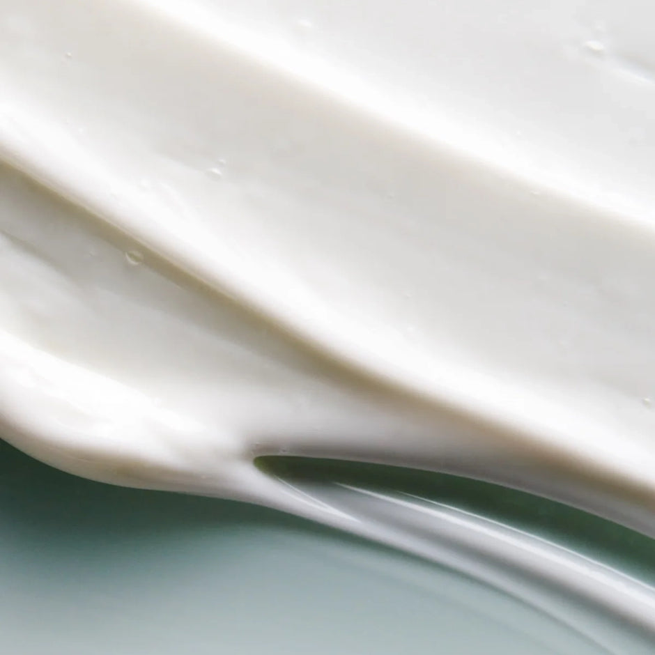 A close-up of a swirled, creamy eye cream texture against a sage green background.
