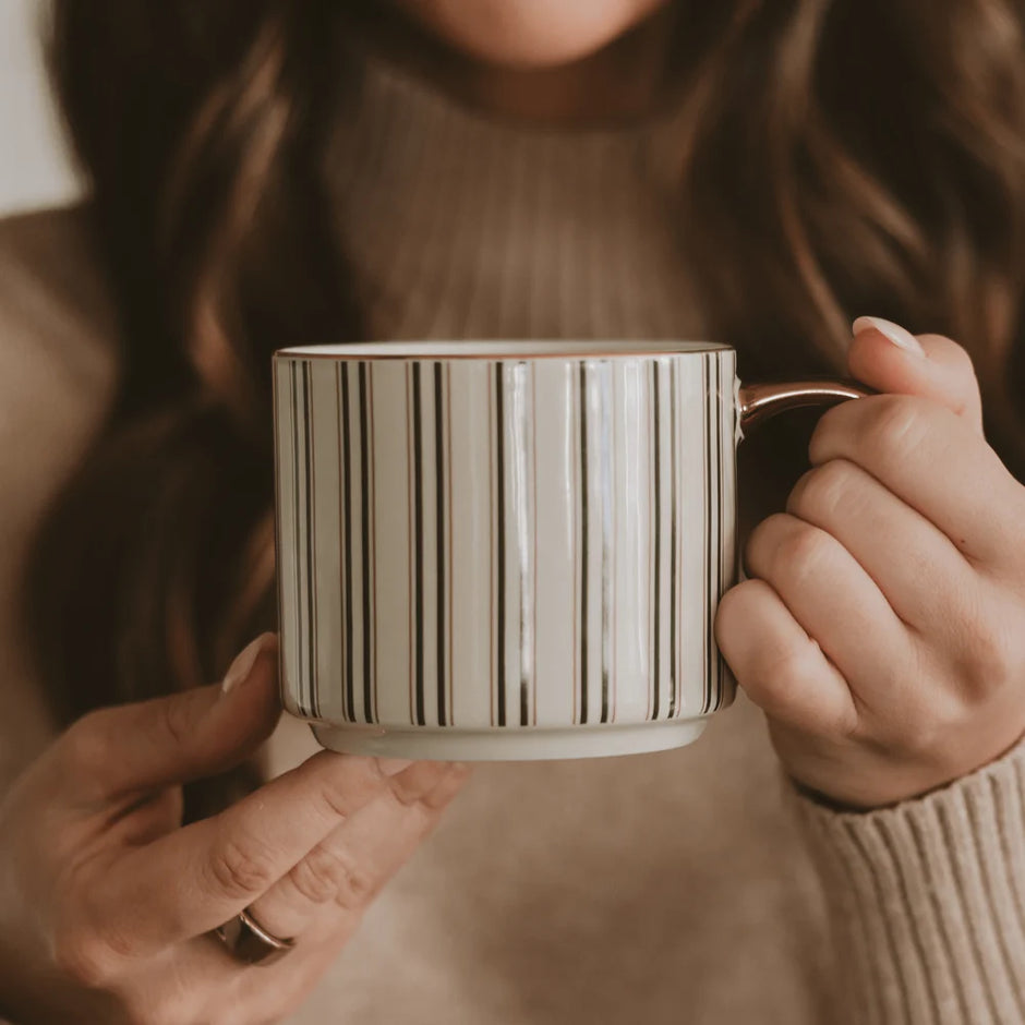 A person holding a ceramic mug with vertical green stripes on a warm beige background.