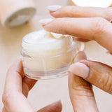 Hands holding an open jar of Dream Slip Overnight Lip Mask, fingertips scooping the creamy balm