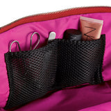KUSSHI | Vacationer Makeup Bag — Candy Apple Red/Pink, Close-up of a bright pink cosmetic bag interior with a black mesh organizer pocket holding scissors, a small tool, a black item, and a pink tube. A red zipper is visible along the top edge.