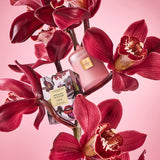 Pink candle and product packaging surrounded by red orchids on a pink background