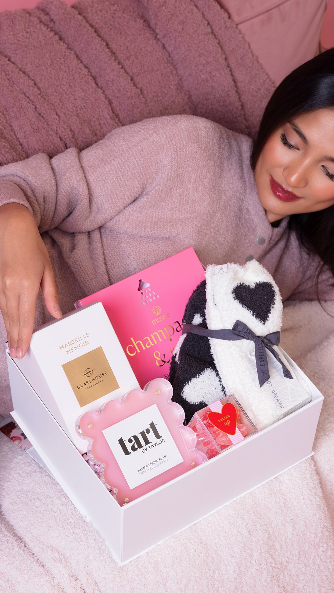 Woman opening a gift box with a cow-themed product and a pink box labeled 'champagne' on a pink couch.