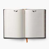 An open lined notebook with black covers on the left and right edges, white lined pages, small black bat decorative illustrations near the top of each page, and an orange ribbon bookmark hanging from the center, shown on a light gray background.
