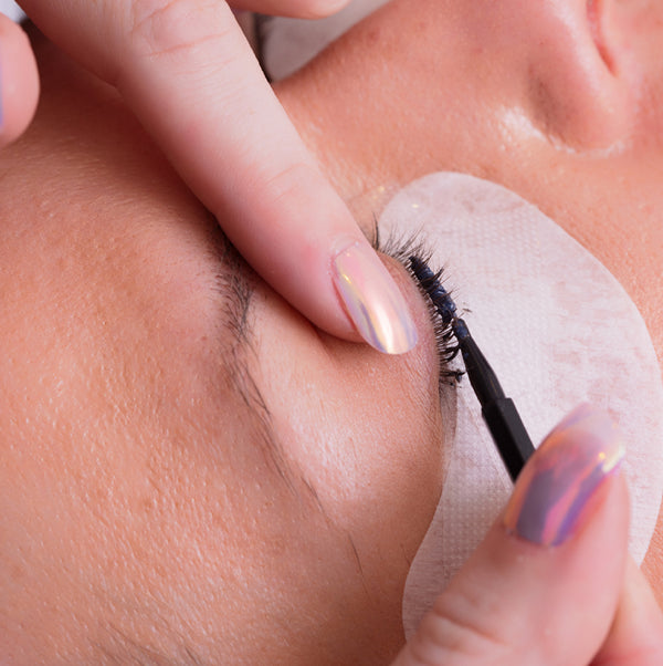 Person applying false eyelashes with a small mirror.