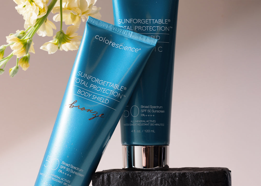 Two bottles of Colorescience Sunforgettable Total Protection sunscreen on a wooden stand with flowers in the background.