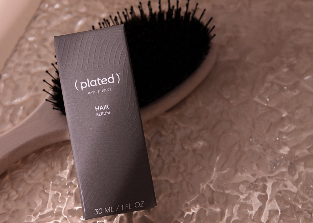 Plated hair serum packaging with a hairbrush on a textured surface