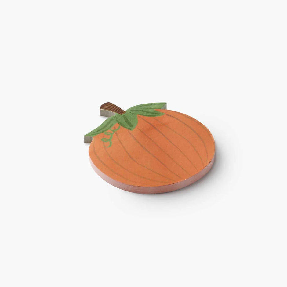 A small pumpkin-shaped pad of sticky notes with an orange body, green leaves, and a brown stem, photographed on a clean white background.