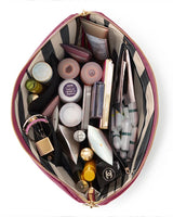 KUSSHI | Vacationer Makeup Bag — Wine/Zebra, An open zippered makeup bag filled with cosmetics and skincare items, photographed from above on a white background. The bag has a pink and black striped exterior and a gold zipper.