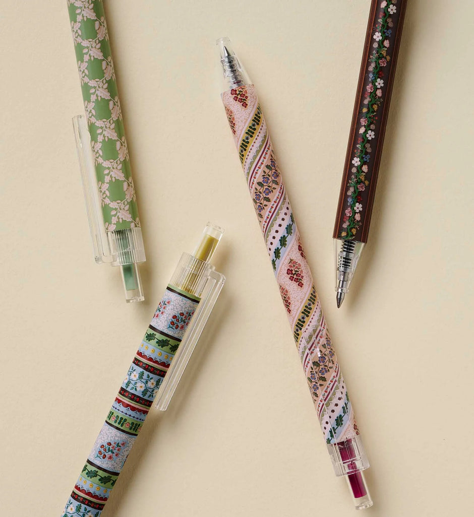 Four decorative gel pens with intricate floral and geometric patterns, arranged diagonally on a warm beige background.