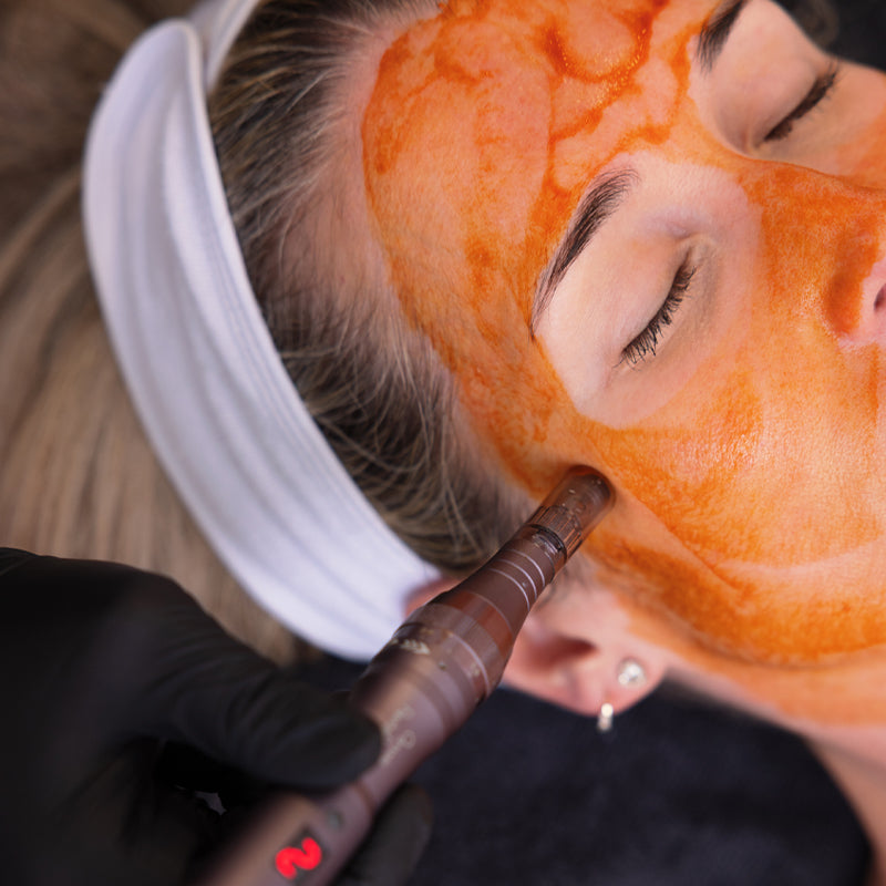 Person receiving a facial treatment with an orange mask and a black-handled tool.