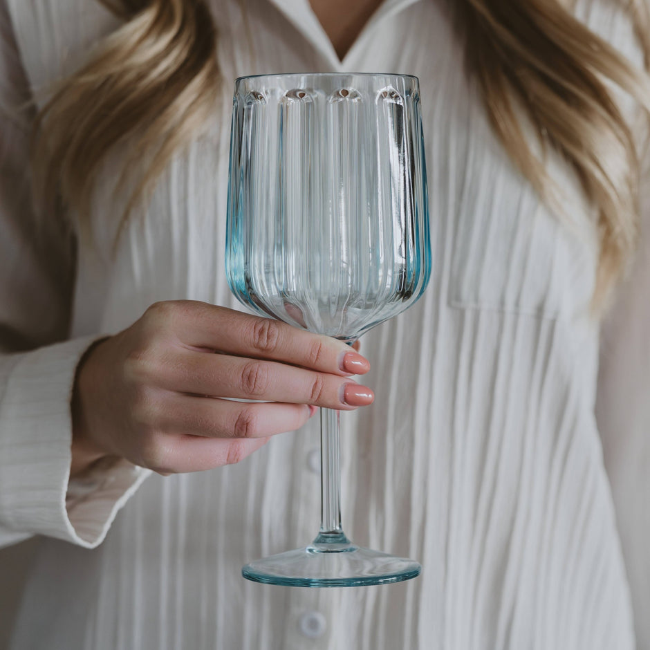 Woman in white shirt holding empty ribbed plastic wine glass against neutral background