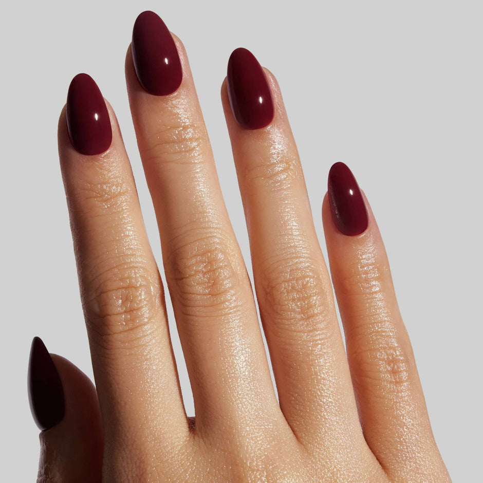 Hand displaying Bordeaux short almond press-on nails with glossy finish against neutral background