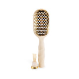 Tan vented hair brush with gold bristles and detachable cleaner tool on black background