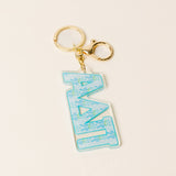 Turquoise floral sorority letter acrylic keychain with gold key rings on neutral background