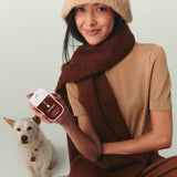 Woman holding Touchland hand sanitizer with dog, wearing beige sweater and burgundy scarf