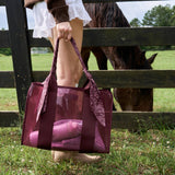 Woman holding burgundy jelly tote bag by wooden fence with horse in background