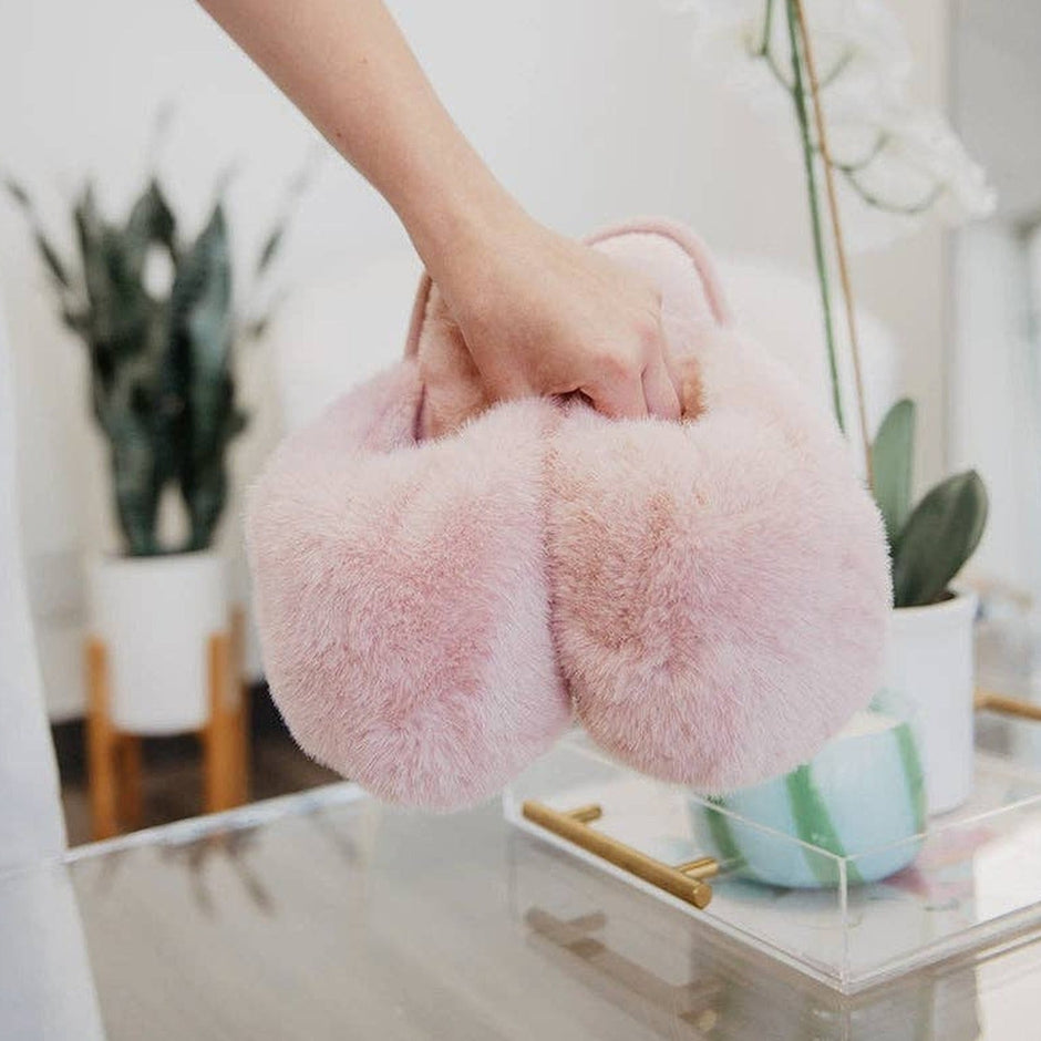 Woman wearing light pink faux fur jumbo slippers in modern home setting with potted plants