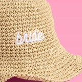 Cream straw bucket hat with white 'bride' embroidery on pink background