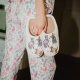 Woman wearing cozy animal-patterned slippers with matching pajamas, holding slippers in hand
