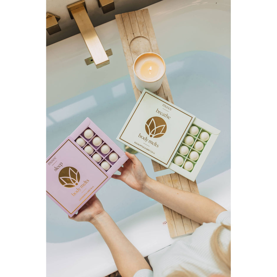 Woman holding Musee sleep body melts in pink packaging with breathe melts and lit candle