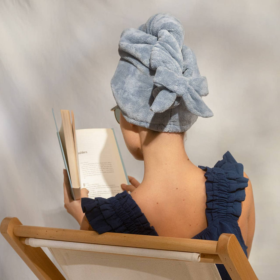 Woman wearing plush microfiber hair towel turban in coastal blue while reading a book