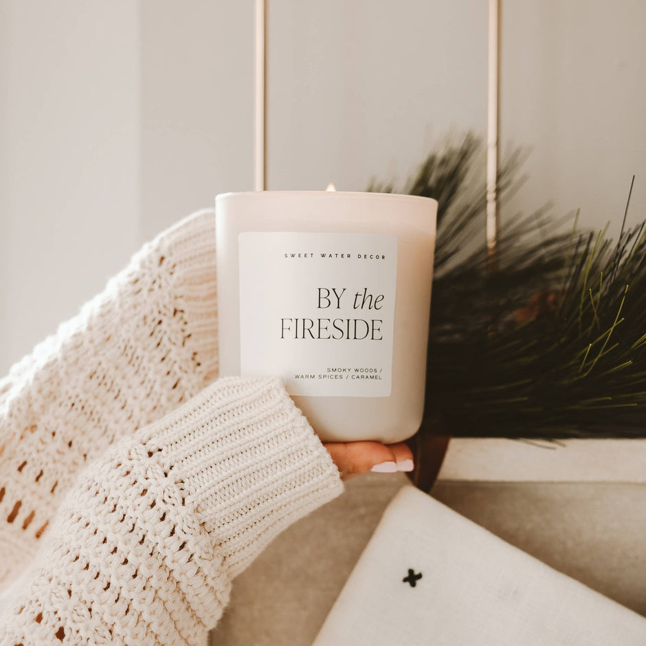 By the Fireside soy candle held in cozy cream sweater with dried grasses and neutral decor