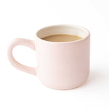 Light pink ceramic coffee mug filled with coffee on white background