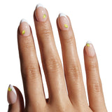 Close-up of a hand with beige nail polish and small yellow dots on a white background