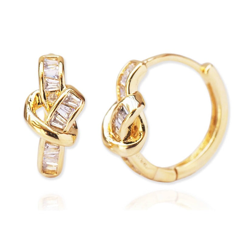 Gold love knot baguette huggie earrings with cubic zirconia stones on white background