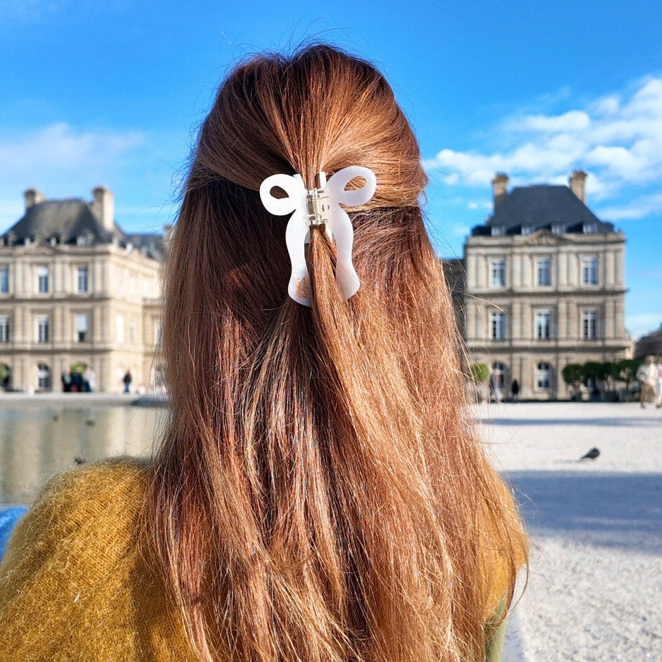 White coquette bow claw clip worn in long brown hair at scenic palace courtyard