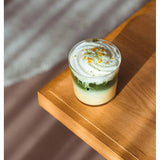 Layered matcha and coconut latte topped with whipped cream in a small glass