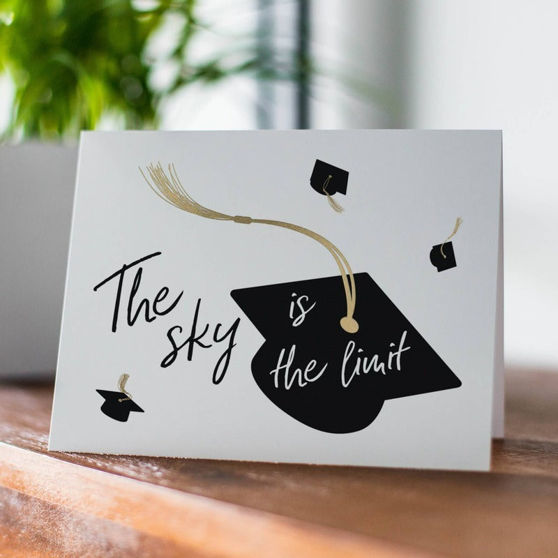 Graduation greeting card with 'The sky is the limit' text and mortarboard design on wooden surface