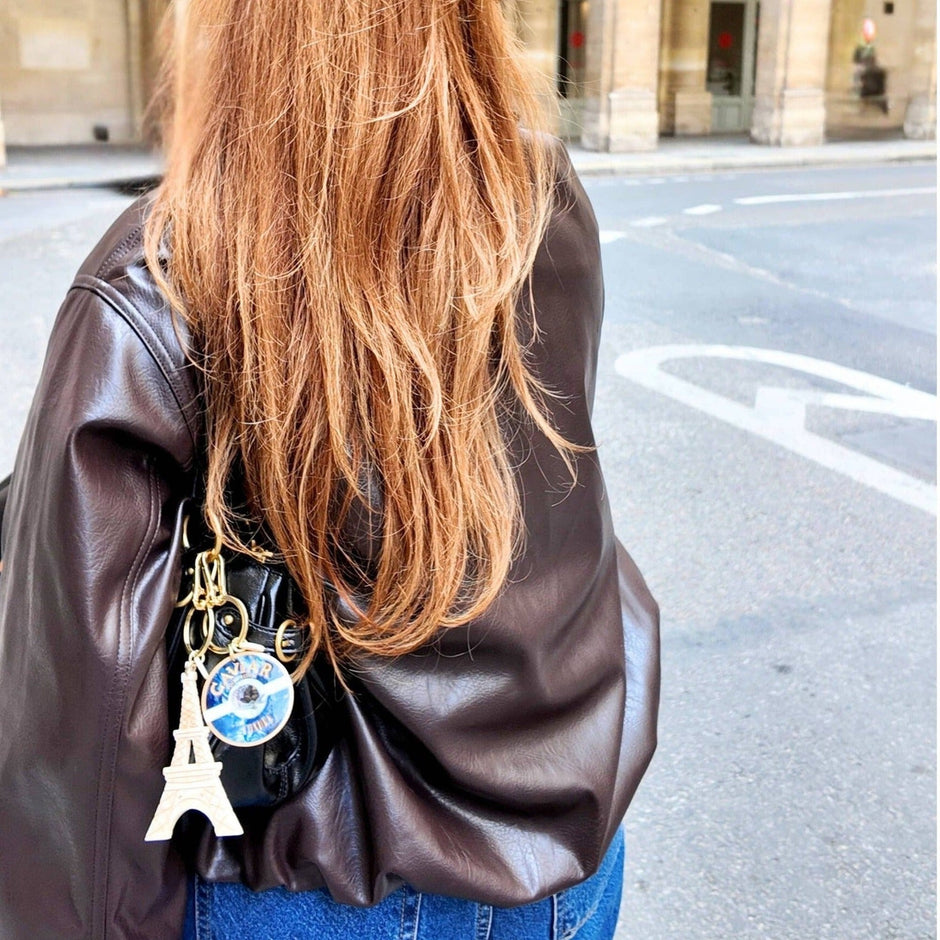 Solar Eclipse bag charm keychain attached to brown leather jacket worn by woman on city street