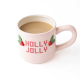 Pink ceramic mug with 'Holly Jolly' text and raspberry design, filled with coffee