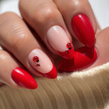 Close-up of a hand with red nail polish and ladybug designs on a beige surface.