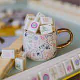Mahjong tiles displayed in decorative coffee mug with floral pattern and gold handle
