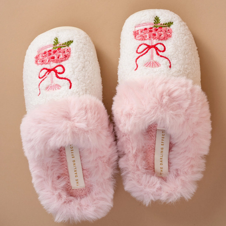 Pair of white slippers with pink fur sole and embroidered design on a beige background
