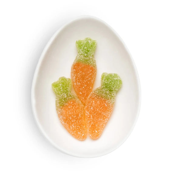 Three carrot-shaped gummy candies on a white plate with a white background