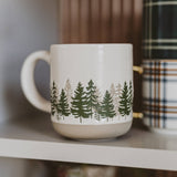 Forest Stoneware Coffee Mug with pine tree design displayed on shelf with books and décor