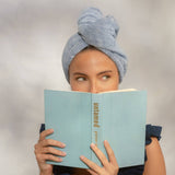 Woman wearing coastal blue microfiber hair towel turban while reading a book