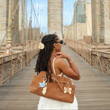 Hand-painted daisy bag charm displayed on brown tote bag worn by woman on Brooklyn Bridge