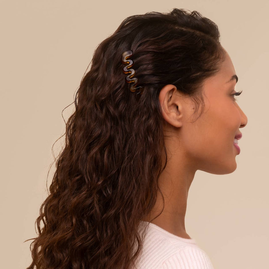 Woman wearing tortoiseshell French hair combs in long wavy brown hair, side profile view